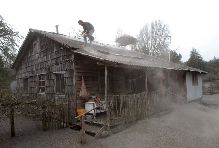 Мужчина расчищает крышу своего дома от пепла после извержения вулкана Кальбуко в Чили