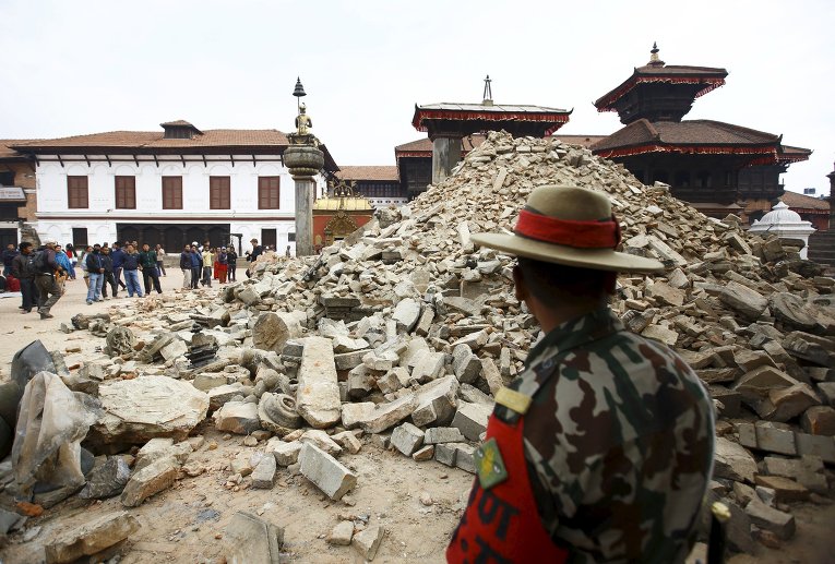 Непальский военнослужащий стоит перед разрушенным храмом