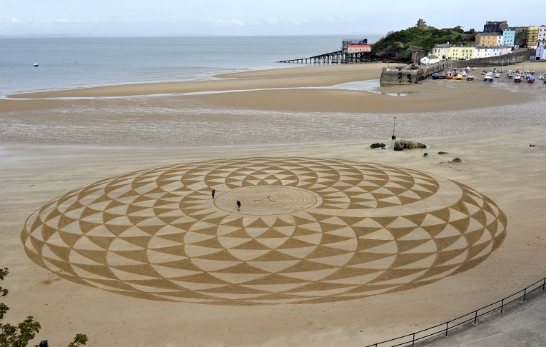 Местные художники рисуют узоры на песке во время отлива на Северном пляже, Тенби, Южный Уэльс.
