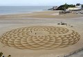 Местные художники рисуют узоры на песке во время отлива на Северном пляже, Тенби, Южный Уэльс.