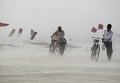 Мужчины едут на велосипедах вдоль берега реки Ганг во время пылевой бури в Аллахабаде, Индия.