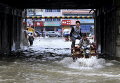 Мужчины едут по затопленной улице под мостом после проливных дождей в Аньшунь, провинция Гуйчжоу, Китай
