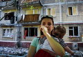 Женщина с ребенком у ее поврежденного в результате обстрелов дома в Горловке