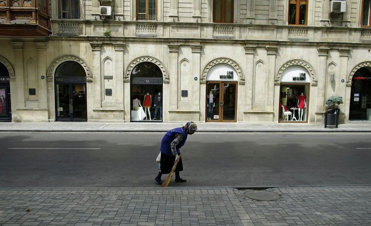 Женщина подметает улицу, где размещены модные бутики в Баку