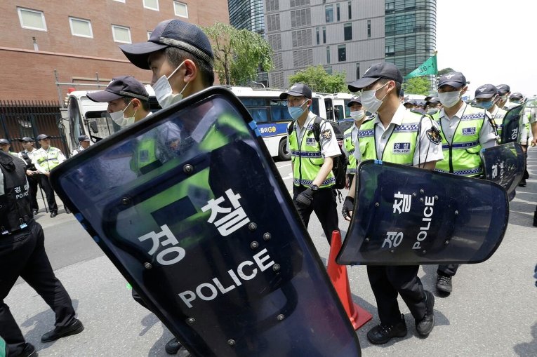 Южнокорейские полицейские в масках, защищающих от попадания микробов коронавируса, перед японским посольством во время митинга, посвященного 50-летию нормализации отношений между Южной Кореей и Японией
