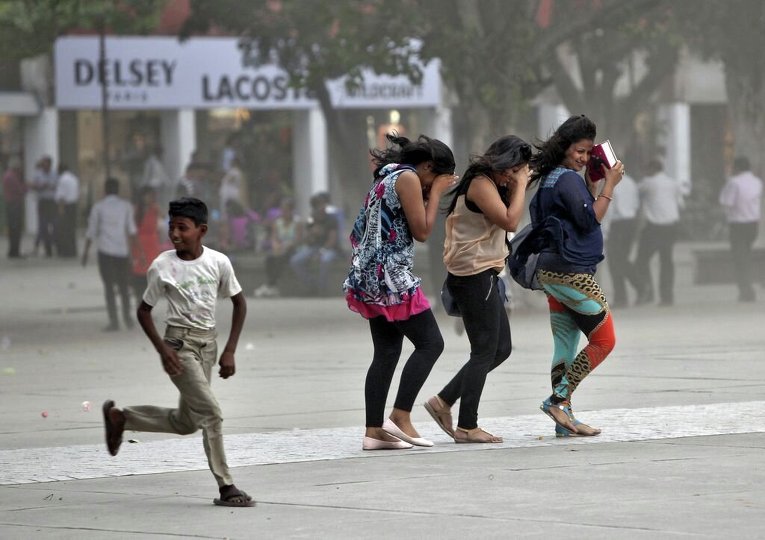 Мальчик бежит рядом с женщинами, пытающимися защитить себя от пылевой бури в Индии
