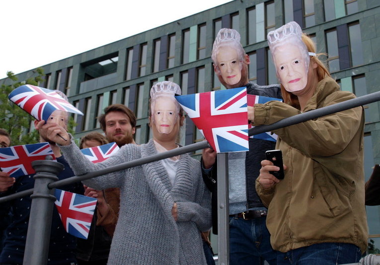 Зрители в масках с лицом британской королевы Елизаветы II с британскими флагами в Берлине