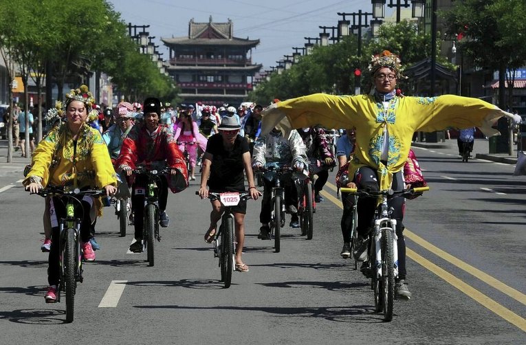 Мужчина в традиционном костюме китайского императора и другие участники акции ездят на велосипедах по улице в Датуне