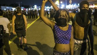 Демонстранты в Фергюсоне, где продолжаются протесты в связи с годовщиной гибели подростка-афроамериканца Майкла Брауна от рук полицейского