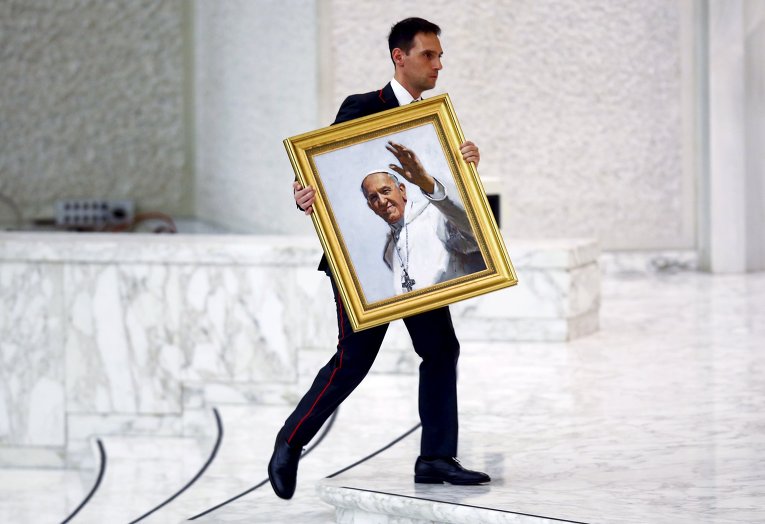 Мужчина несет картину, изображающую Франциска во время общей аудиенции в Ватикане