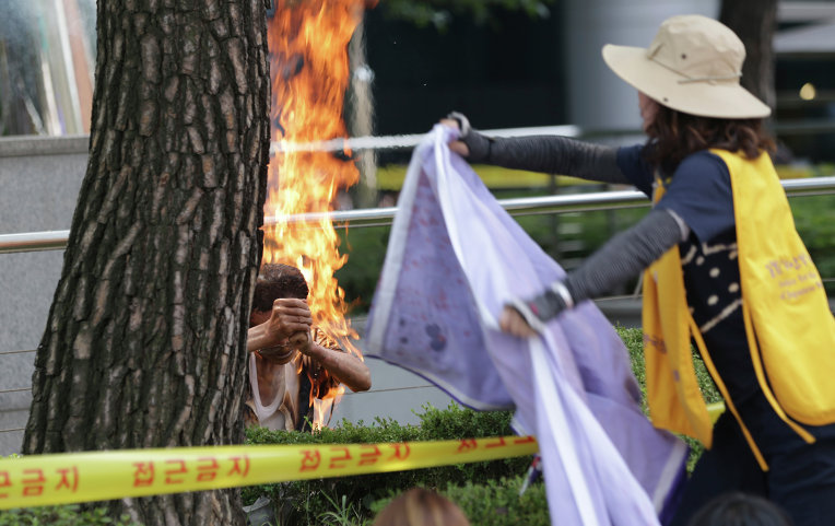 Женщина пытается потушить мужчину, устроившего самосожжение на митинге перед посольством Японии в Сеуле