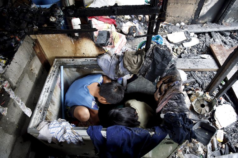 Филиппинские дети мародерничают на обломках дома, сгоревшего в результате пожара в одном из спальных районов Манилы.