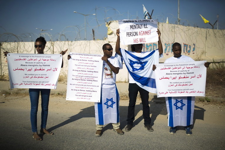 Демонстранты держат плакаты и флаги с призывом освободить Авраама Менгисто на КПП Эрез на юге Израиля, недалеко от сектора Газа