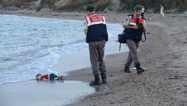 Турецкие полицейские рядом с телом маленького сирийского мигранта, который утонул вместе с другими мигрантами, когда их лодка перевернулась.