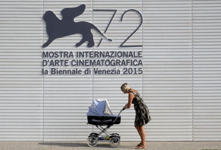 Женщина везет коляску на фоне логотипа 72-ого Венецианского кинофестиваля.