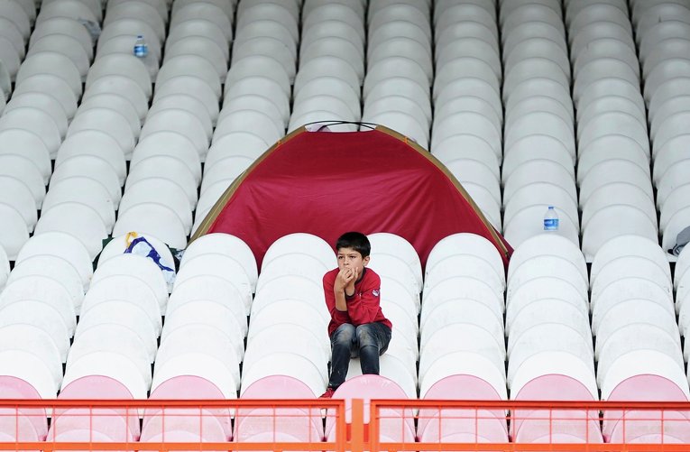 Маленький сирийский беженец сидит на трибунах спортивного стадиона в Турции в ожидании своей очереди, чтобы отправиться в Болгарию или Грецию.