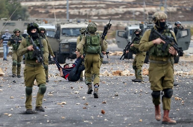 Израильские солдаты уносят раненного палестинца, который пострадал во время столкновений в Рамалле