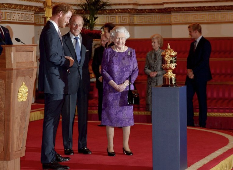 Принц Гарри, герцог Эдинбургский и королева Елизаветта в Букингемском дворце смотрят на Кубок Уэбба Эллиса, вручаемый команде, победившей на чемпионате мира по регби
