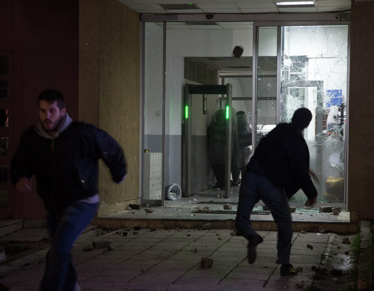 Протестующий бросает камни в полицейских, которые укрылись внутри центрального РУВД в Косово в Приштине