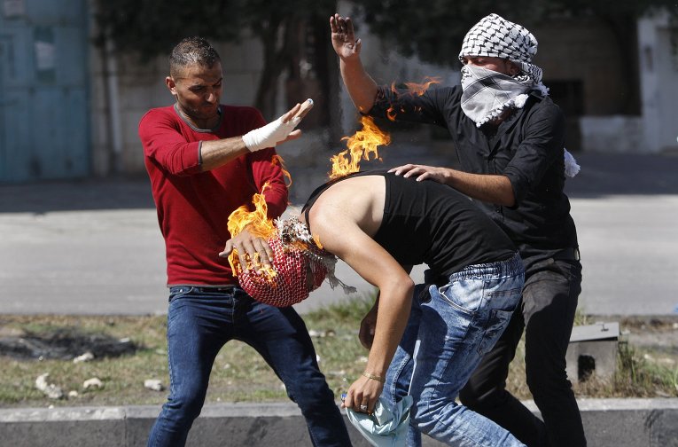 Палестинский протестующий неудачно бросил коктейль Молотова в израильских полицейский и подпалил себя, на фото - товарищи оказывают ему помощь