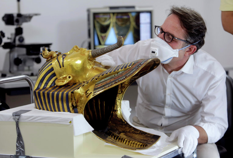 Немецкий реставратор Кристиан Экмана рассматривает бороду золотой маски знаменитого египетского фараона Тутанхамона перед началом реставрационных работ
