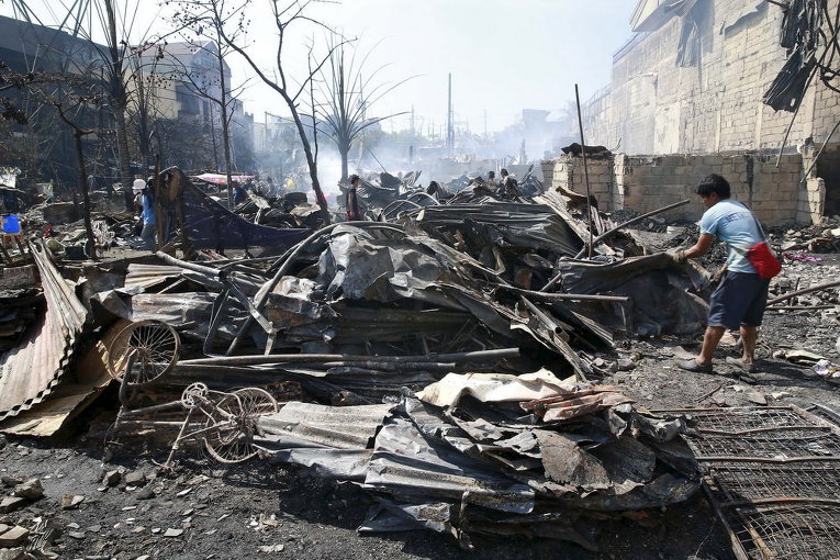 Жители ищут вещи в своих сгоревших домах после пожара в трущобах в городе Кесон, Манилы